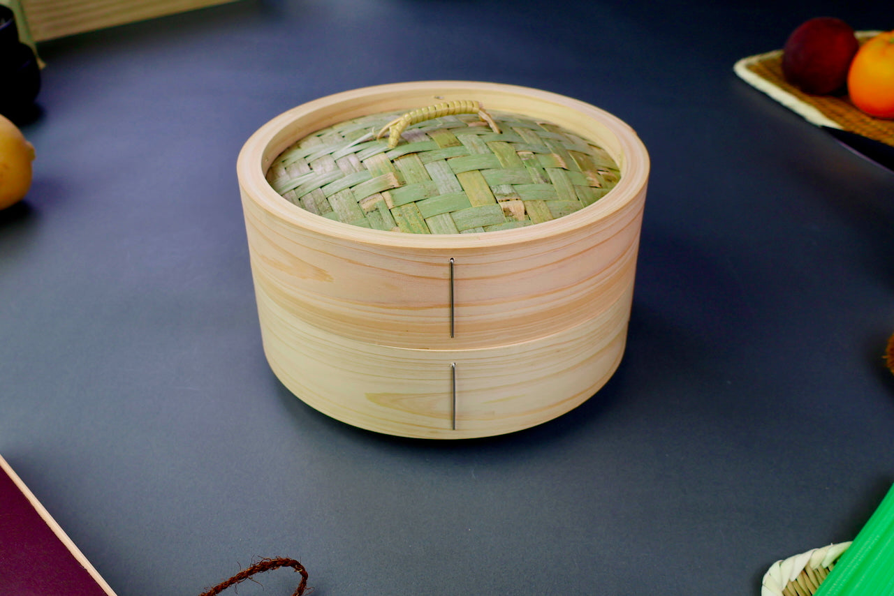 thick wood round bamboo steamer set woven top with loop natural wood tone with printed hiragana surrounded by japanese kitchenware blue gray background