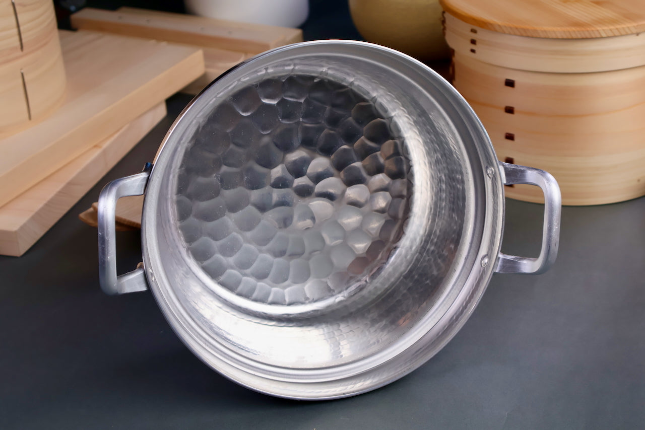 hammered aluminum cooking pot with curved ledge for bamboo steamer two handles 21cm surrounded by kitchenware gray background