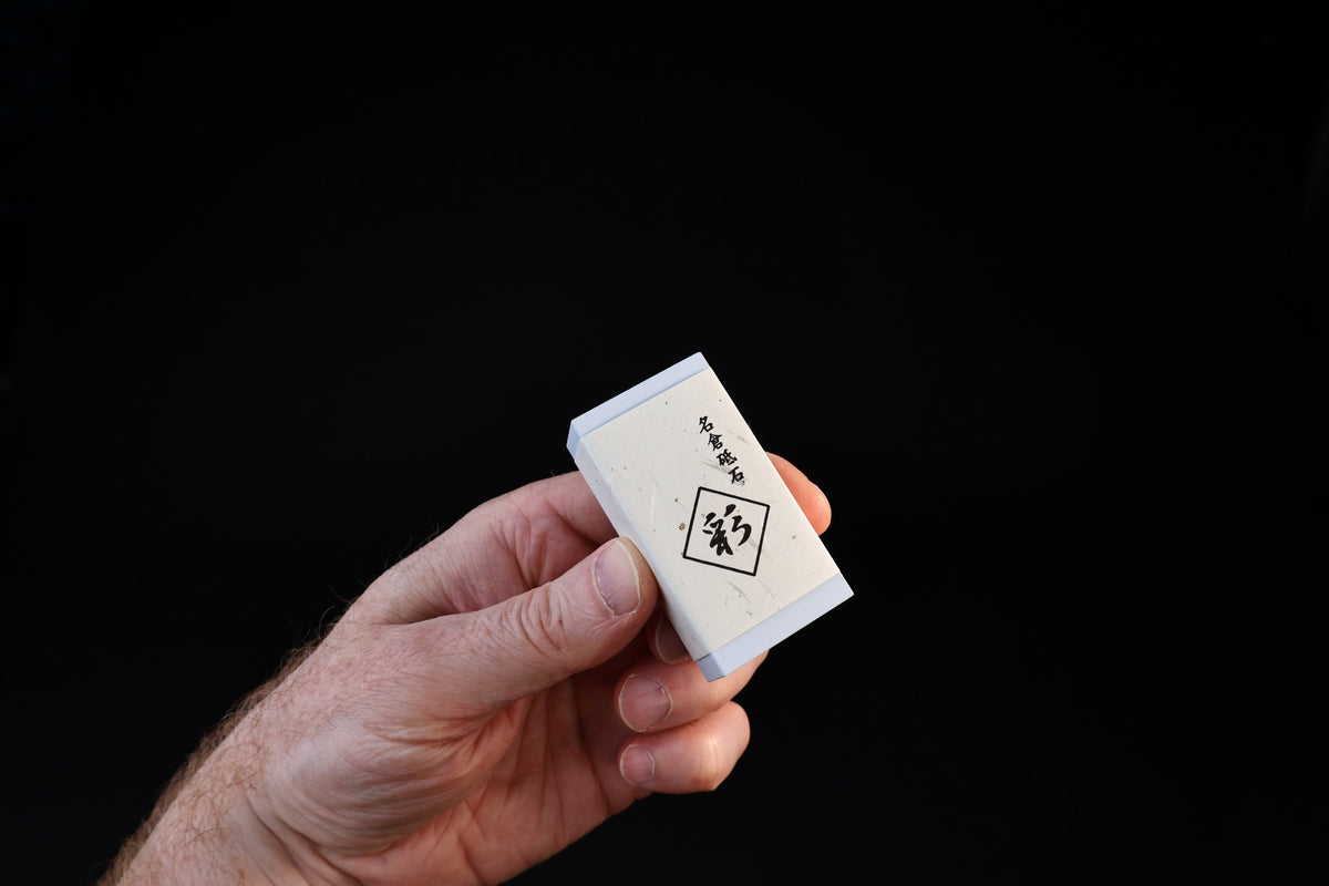 Naniwa Nagura stone with blue-gray ends held in hand, 名倉砥石 label and Sai mark visible