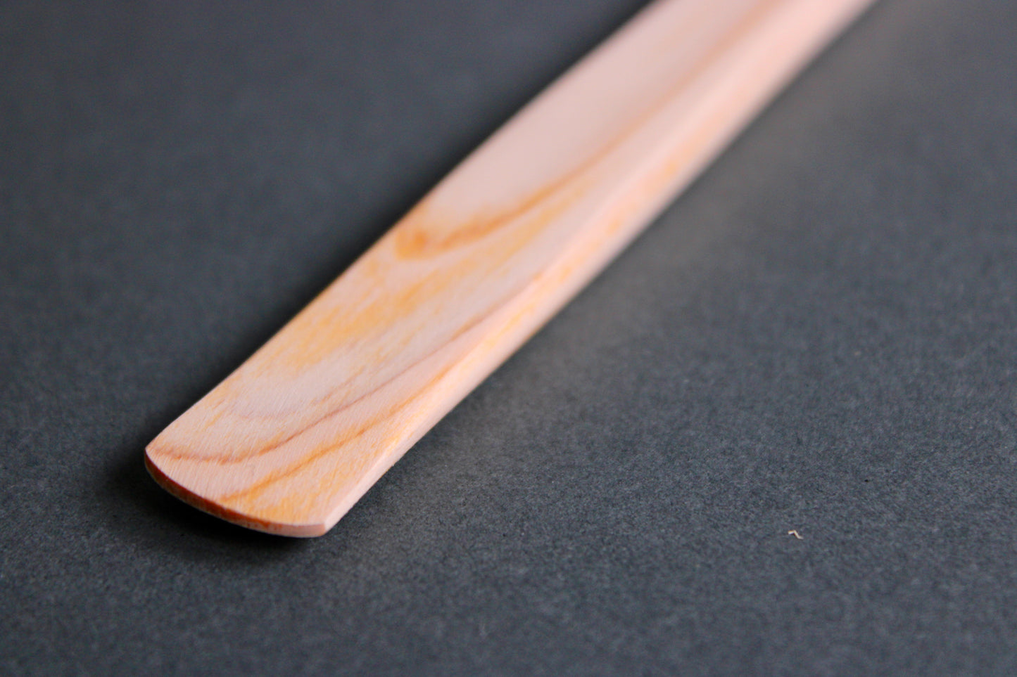 long thin flat natural wood tone hinoki spreader in dark grey backdrop