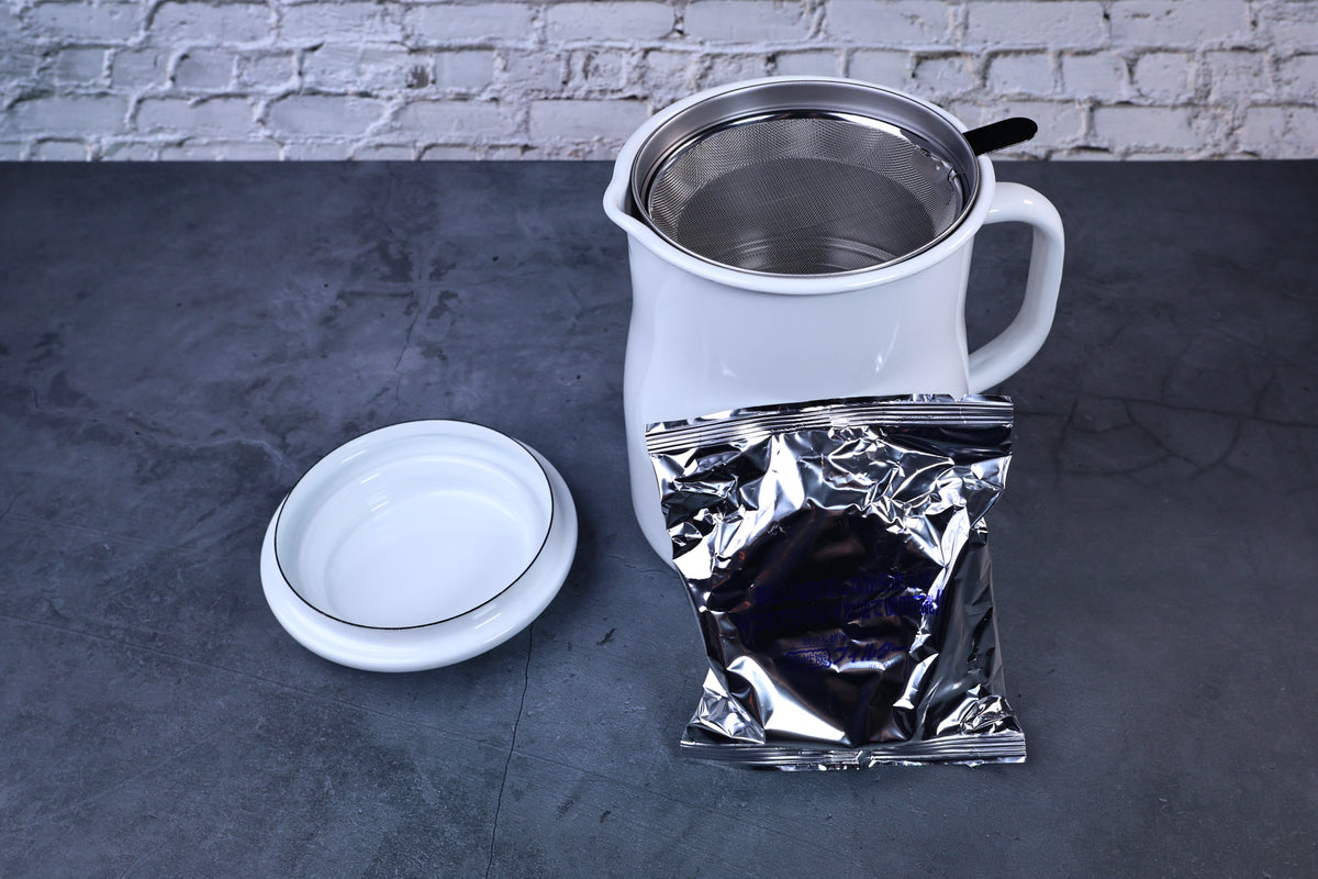 Noda Horo enamel oil pot — open showing filter and included charcoal refill packet alongside pot