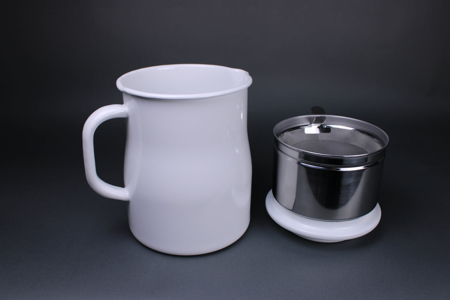image showing white glazed oil pot pitcher with large handle aluminum insert holding filter tray sitting atop white glazed lid which doubles as a rest for easy oil cleanup there is a grey background contrasting the bright product