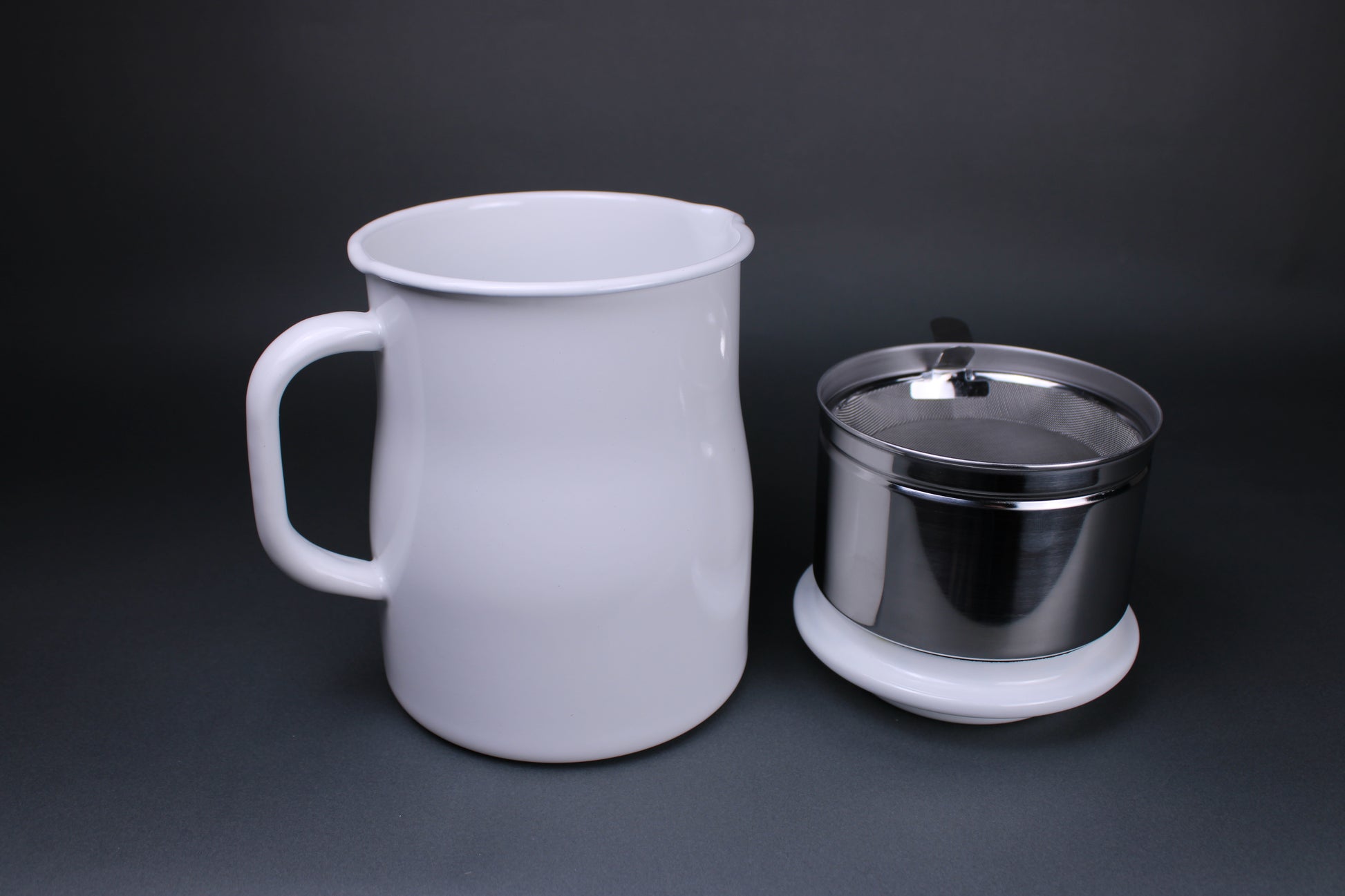 image showing white glazed oil pot pitcher with large handle aluminum insert holding filter tray sitting atop white glazed lid which doubles as a rest for easy oil cleanup there is a grey background contrasting the bright product