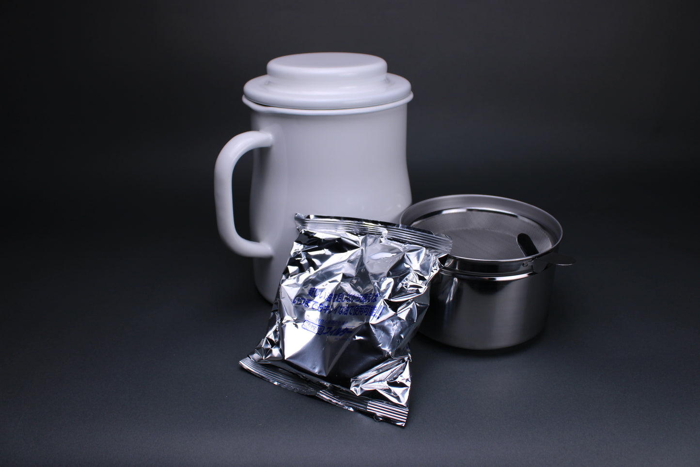 frontal image showing noda horo oil storage pot with aluminum insert holding strainer and filter for oil oil pot is glazed a deep white with sturdy hands and lid also used to hold insert for cleanliness sitting in front of dark grey background