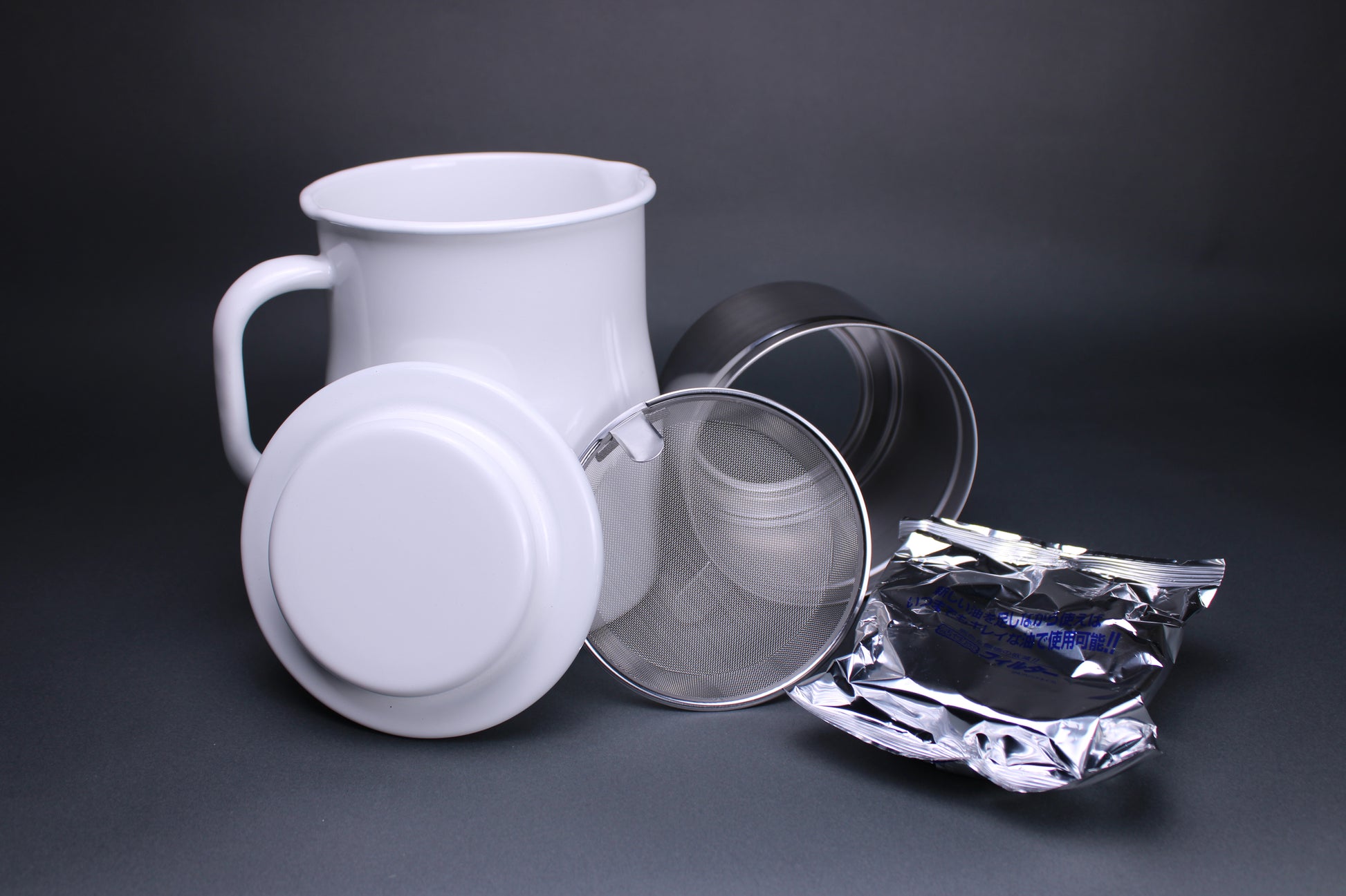 frontal product image showing all the accessories including the white glazed oil pot white glazed deep curved lid insert piece and filter screen and carbon filter to strain oil there is a grey background contrasting the products