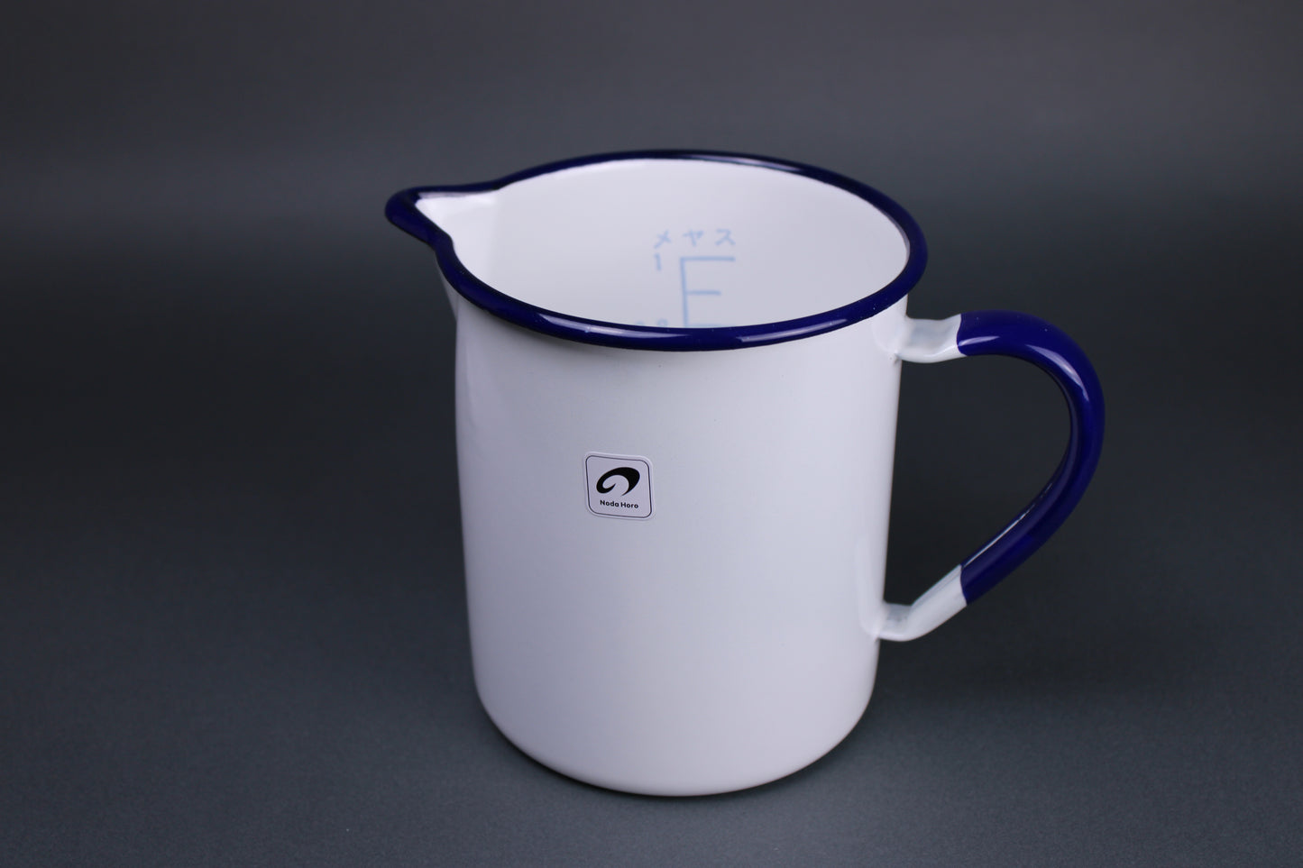 frontal view of noda horo one liter measuring cup with white glazed body navy blue glaze on the handle and the rim of the pitcher with grey background