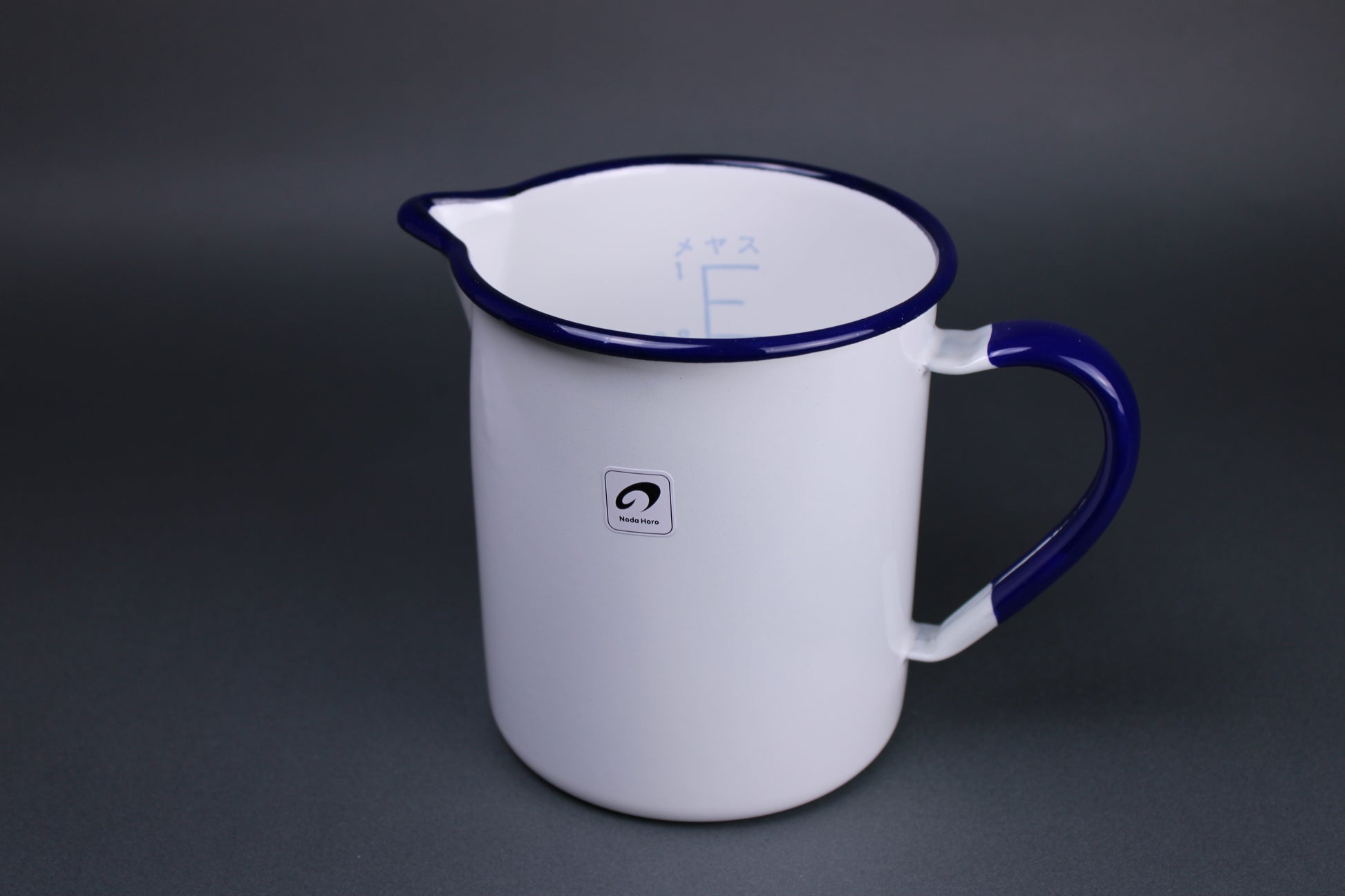 frontal view of noda horo one liter measuring cup with white glazed body navy blue glaze on the handle and the rim of the pitcher with grey background