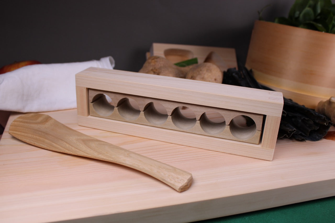 onigiri rice ball maker with barrel shape for bento atop hinoki kitchen craft cutting board okubo house rice scoop with kitchen background