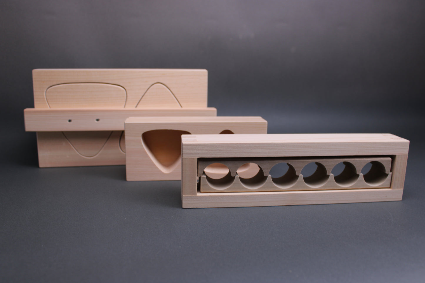 three variously sized and shaped onigiri molds made of hinoki wood tan wood tone in dark grey backdrop