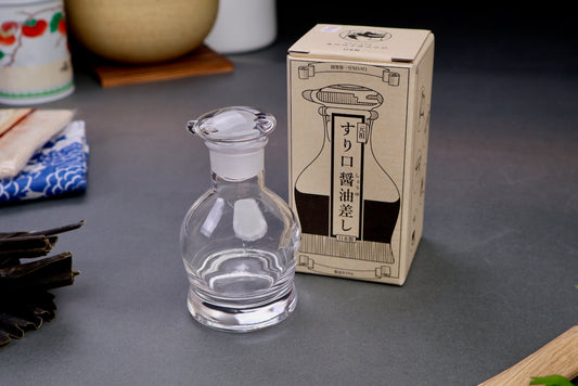 hirota glass original soy sauce cruet bulbous short body with circular lid next to tan white product box hiragana characters and animation with grey backdrop