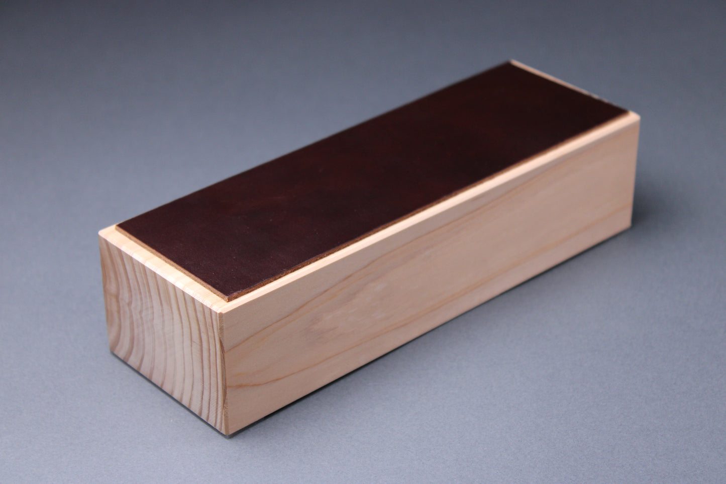 english bridle leather knife strop colored pecan deep brown mounted to tall hinoki wood yoshino base with smooth sides showing tree rings with light grey background profile shot