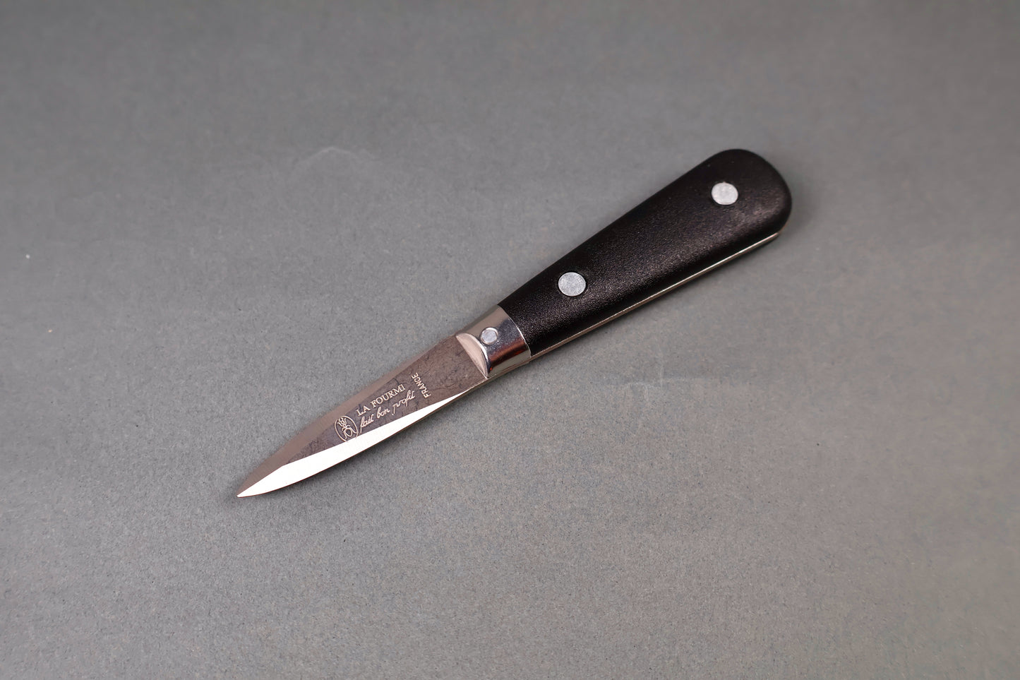 black handled stainless steel beveled oyster knife printed with French writing on grey surface