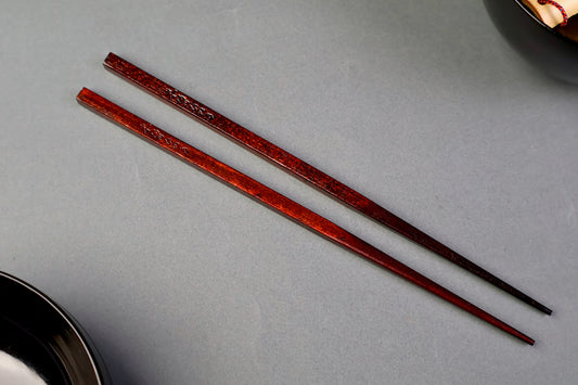 top down shot of two hinoki wood chopsticks with hiragana engraving urushi dark brown coating in light grey background