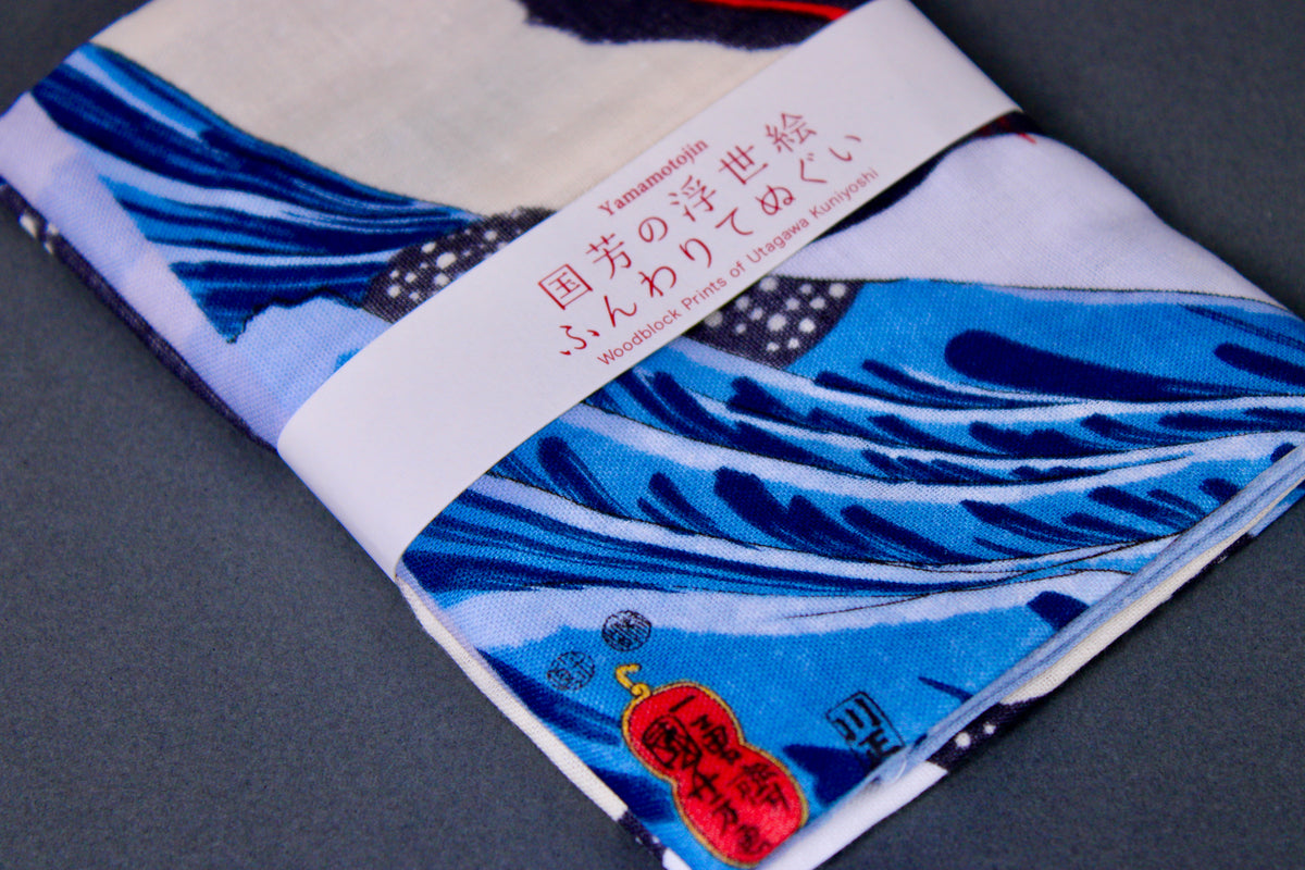 rectangular packaged tenugui towel printed with blue red black classical japanese whale on dark backdrop