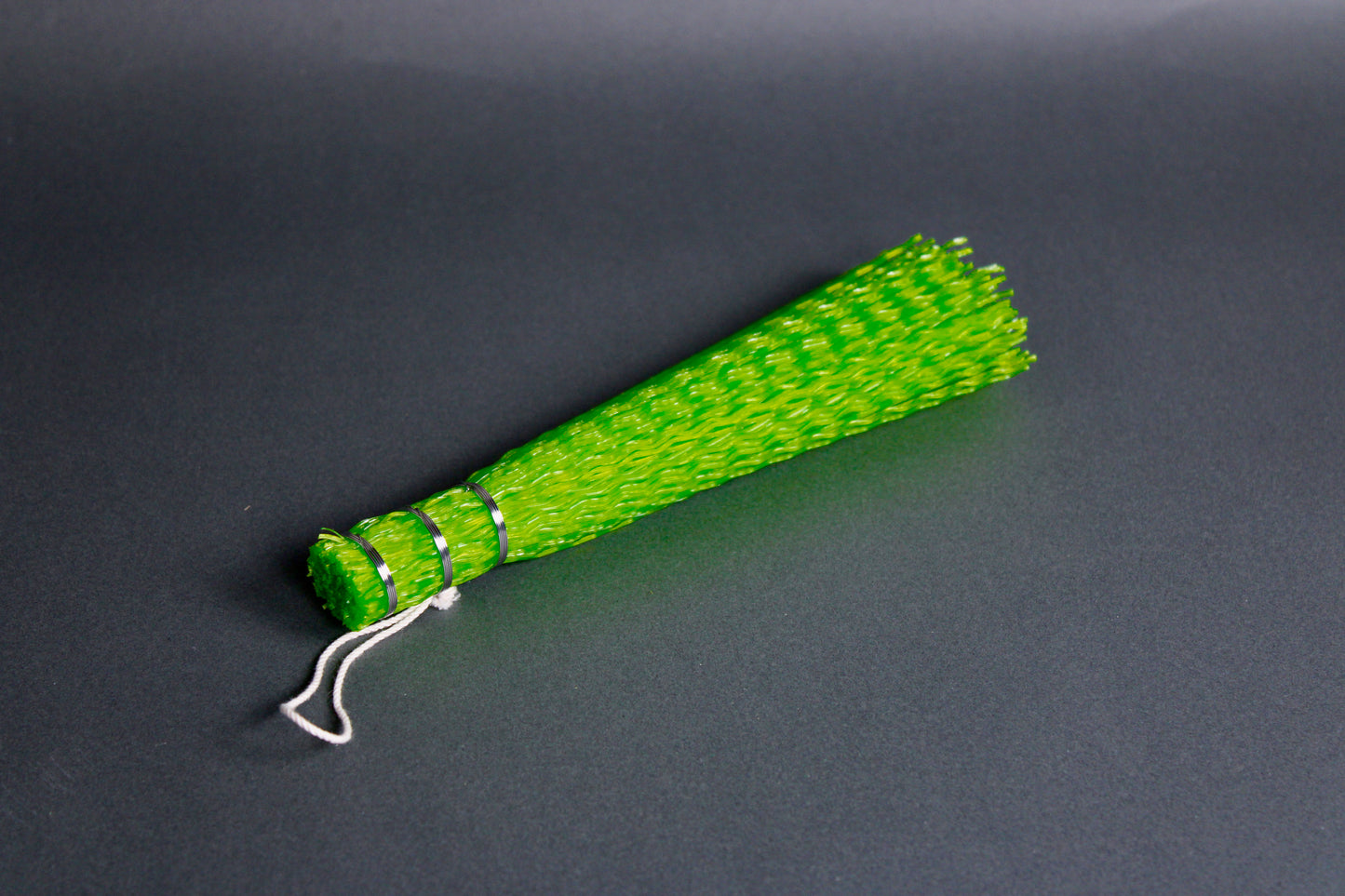 long thin bright green bristly coarse brush wrapped at one end taut with stainless steel wire looped twine on top of gray surface