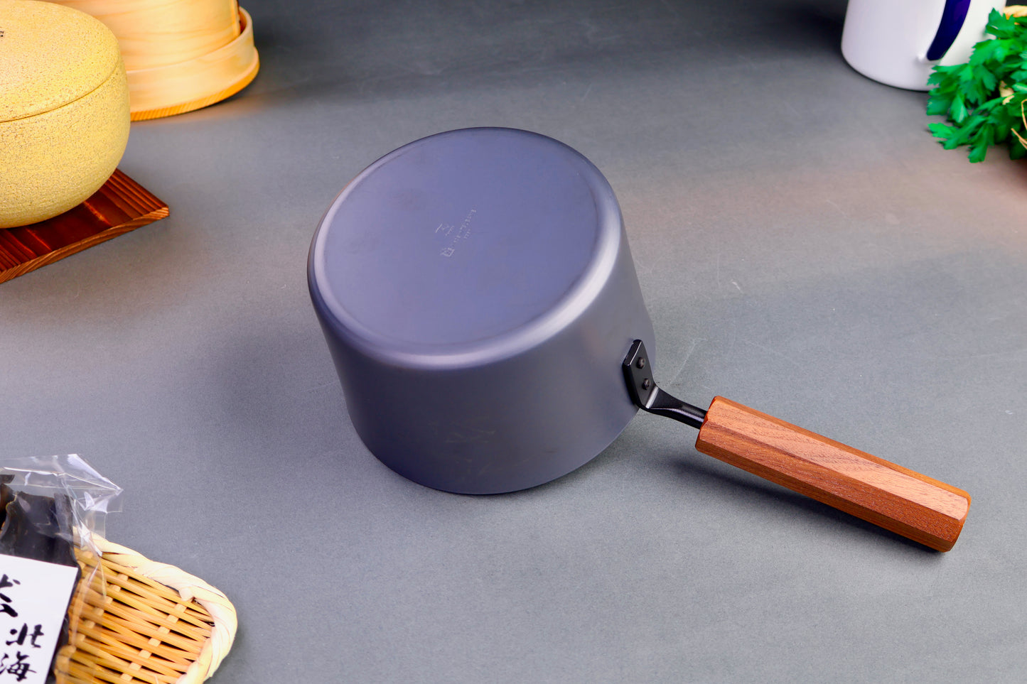 underside of saucepan with wood octagonal handle surrounding kitchenware grey background