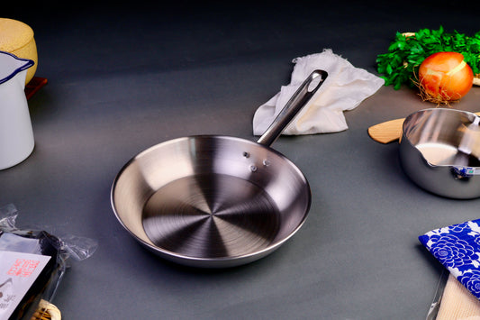 high quality stainless steel saute pan with long elegant handle surrounded by Japanese kitchenware with light grey background