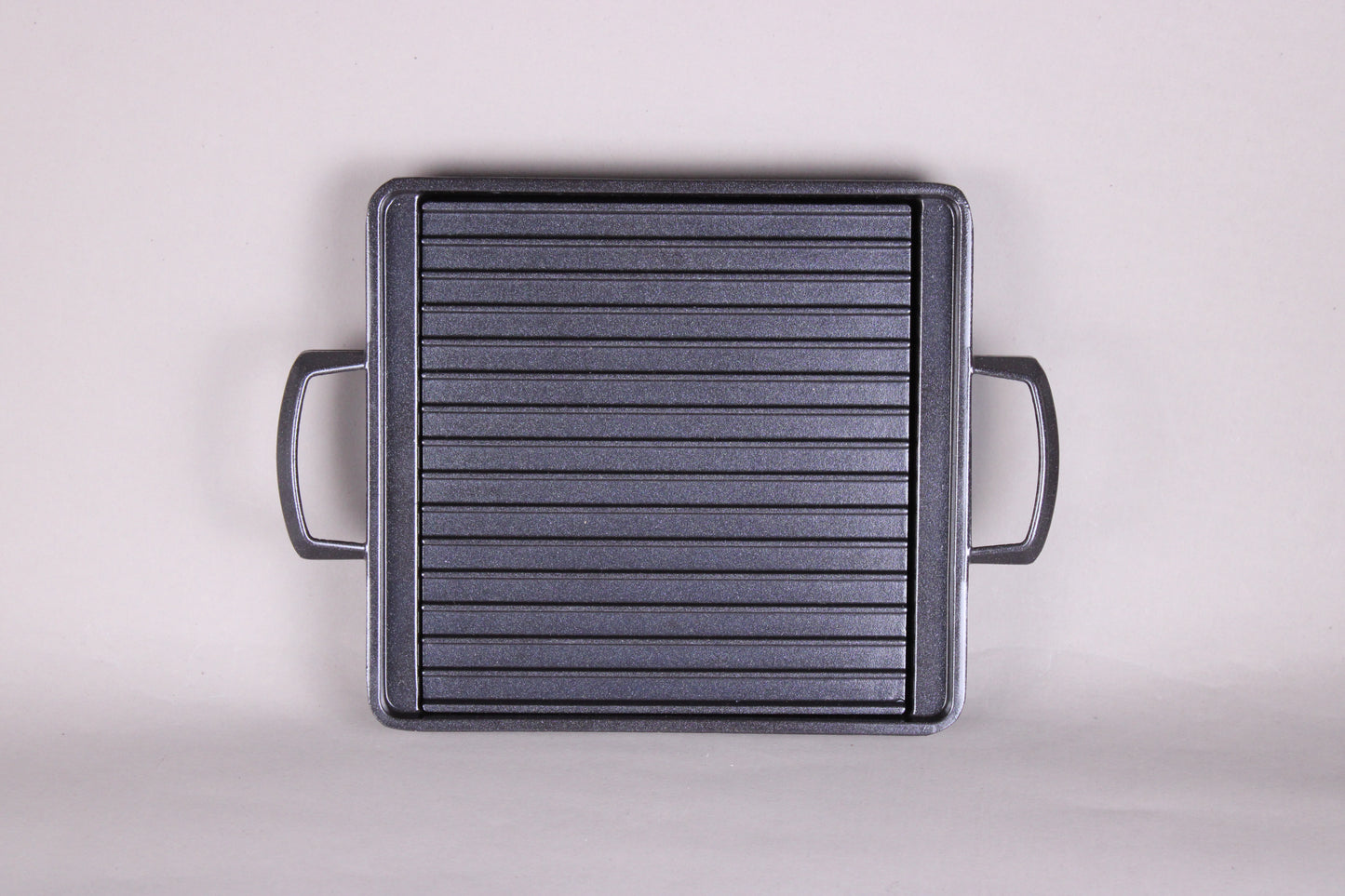 square black grill with 2 handles ridges and removable center plate shown with grey background