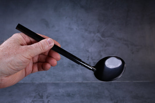 Stainless steel oxidized ladle — octagonal wooden handle grip and solid blackened bowl held in hand