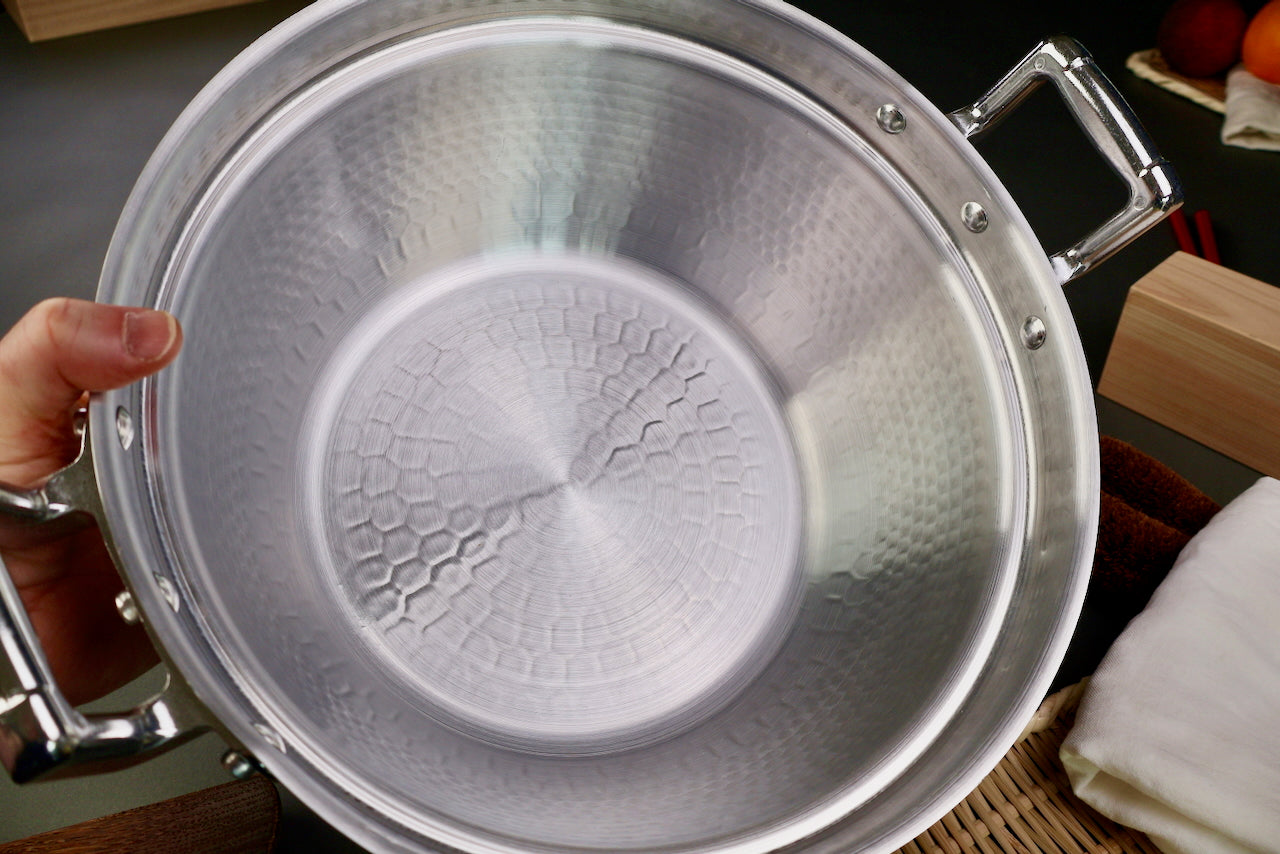 hand holding close up interior of two handled stepped aluminum silvery pot with shiny hammered surface