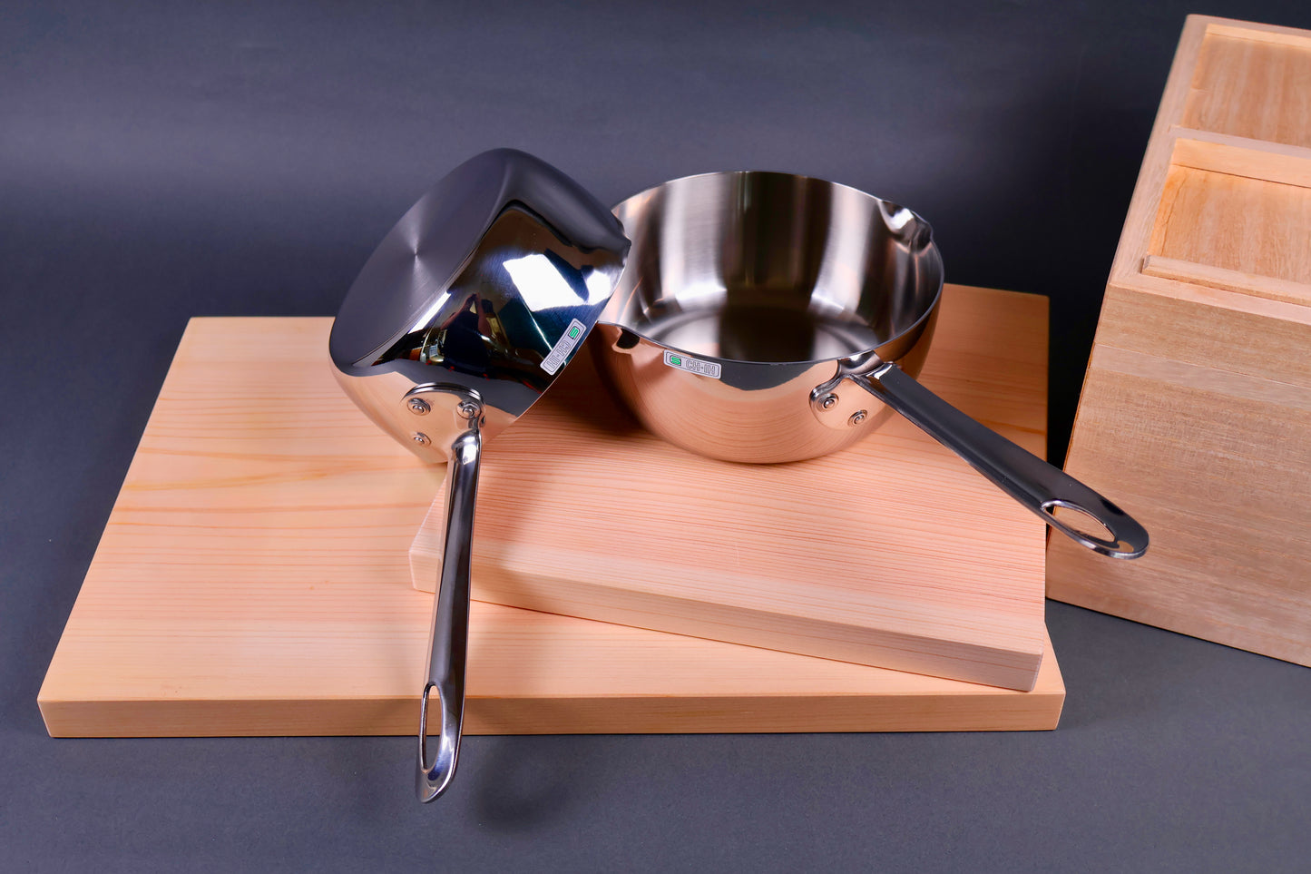 top down image of two japanese saucepans one leaning on the other on top of wood cutting boards in grey background