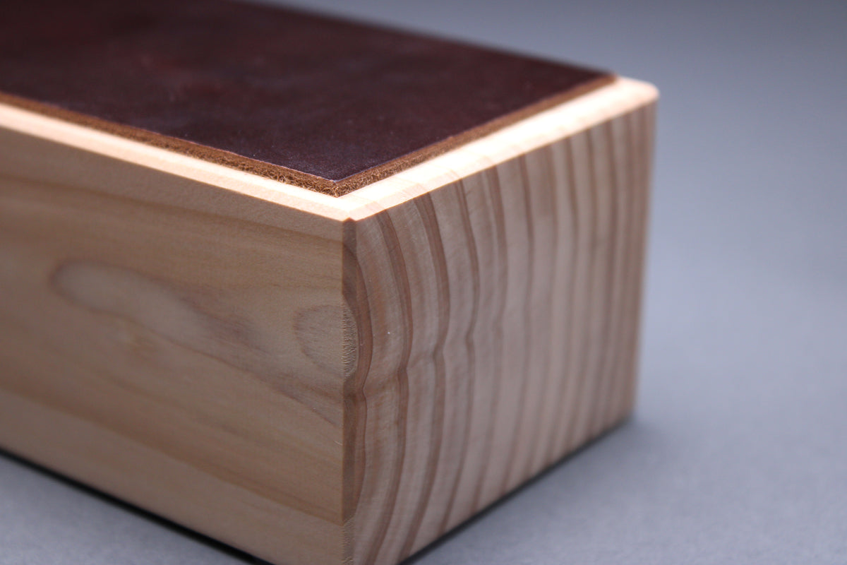 thick strip English bridle leather showing unique pecan deep brown color and natural leather color atop tall sturdy hinoki wood base and light grey background detailed closeup