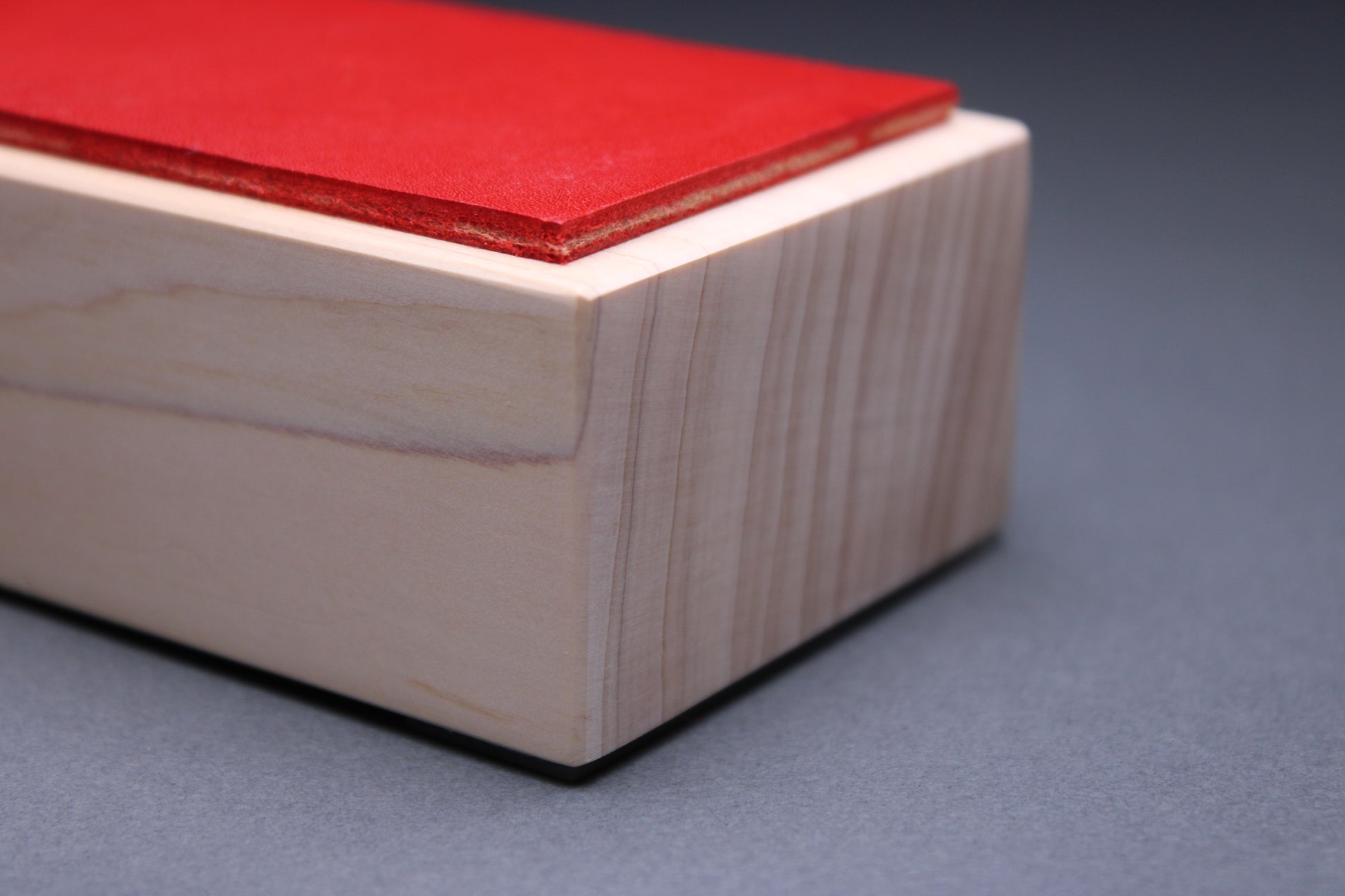 thick strip English bridle leather showing unique deep vermilion red color and natural leather color atop tall sturdy hinoki wood base and light grey background detailed closeup