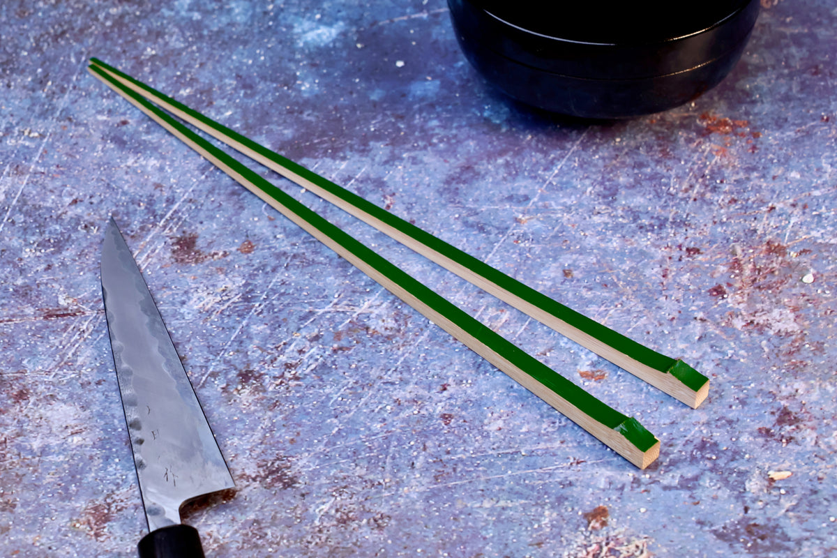 Tenbushi dark green bamboo chopsticks on textured surface with Japanese knife and lacquer bowl, styled kitchen scene