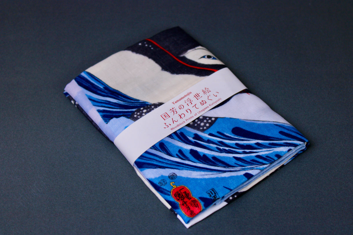 rectangular packaged tenugui towel printed with blue red black classical japanese whale on dark backdrop