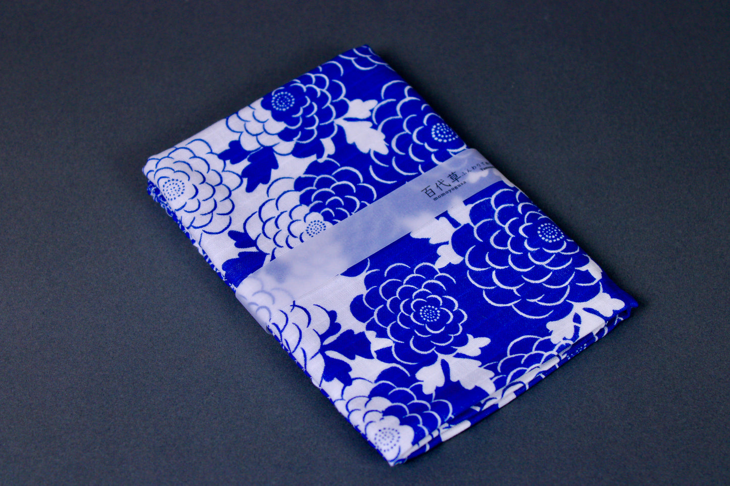 rectangular packaged tenugui towel printed with blue white classic floral pattern on dark backdrop
