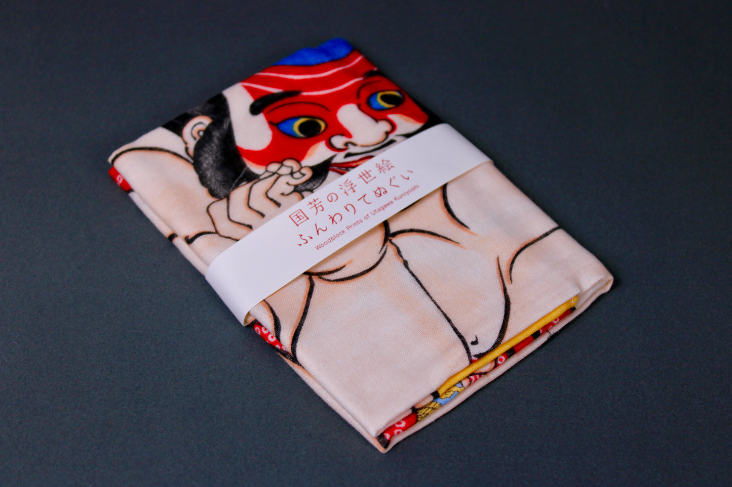 rectangular packaged tenugui towel printed with blue red tan black classical japanese warrior on dark backdrop