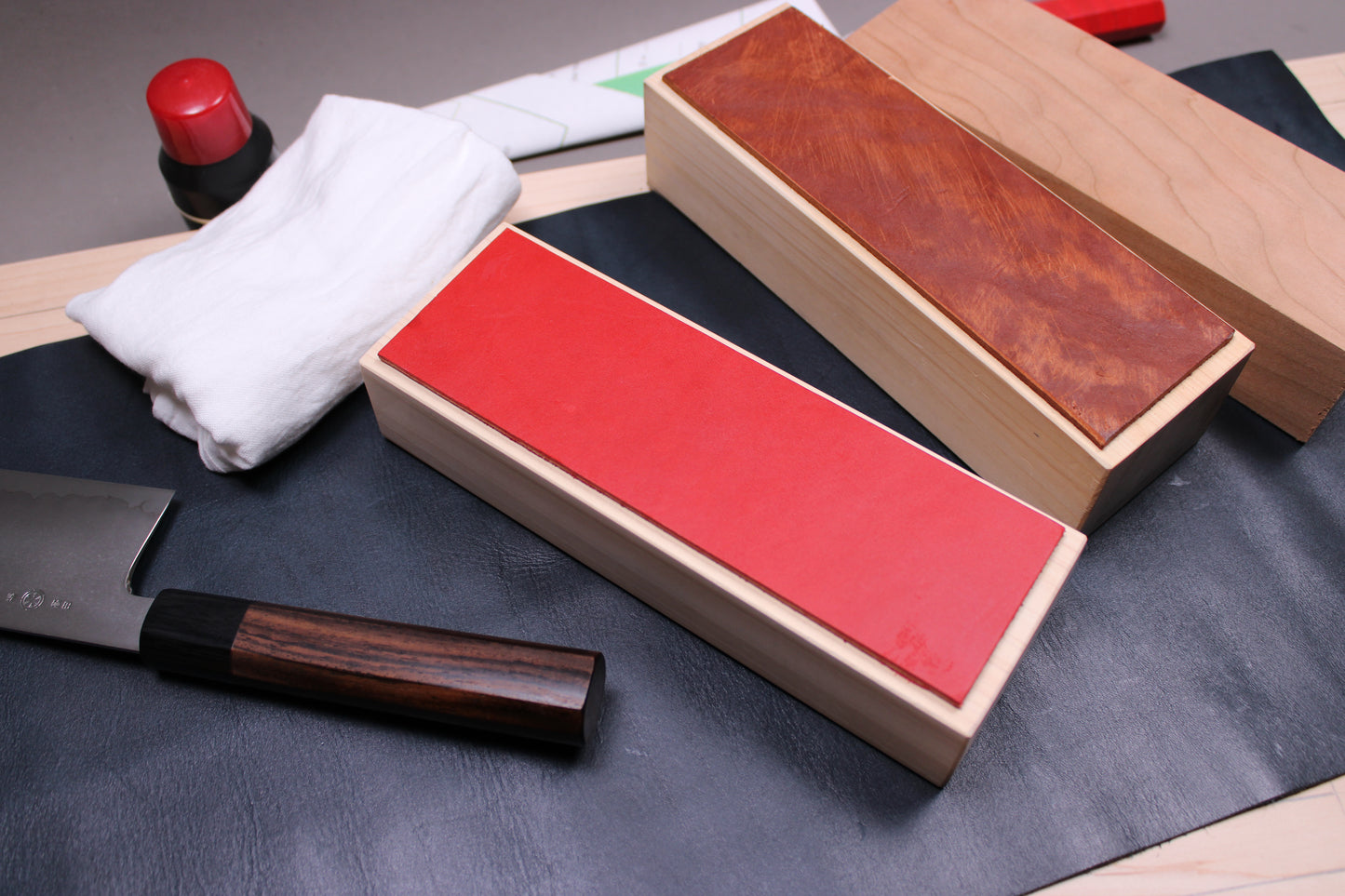 vermilion leather knife strop by hinoki kitchen knife craft surrounded by takada no hamono nakiri sarashi towel morihei oil stick Konosuke hd2 gyuto with workshop background