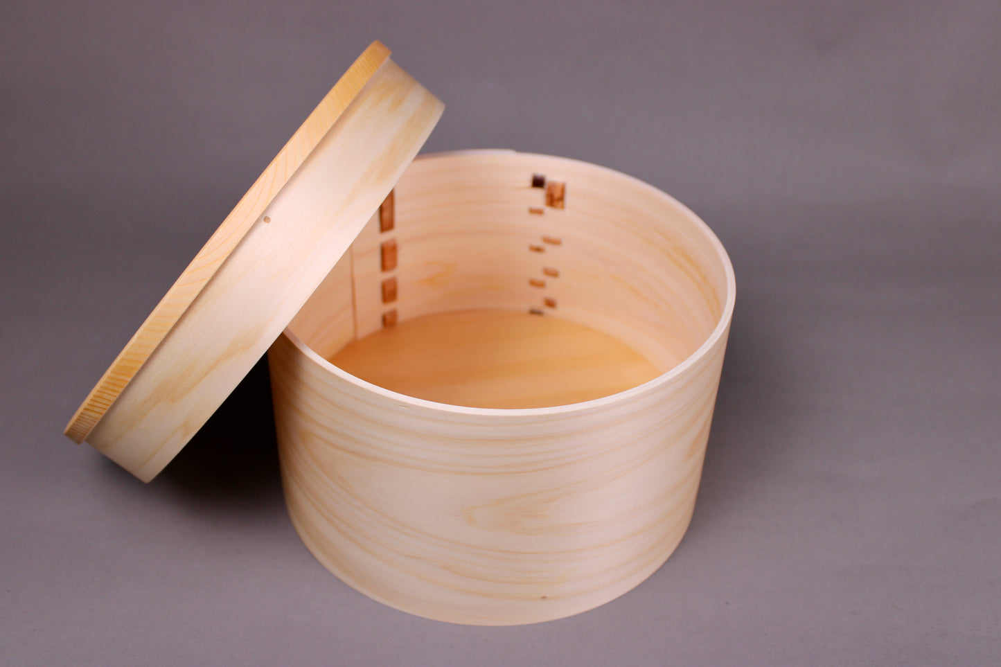 round hinoki wood container with lid leaning against body in dark grey background