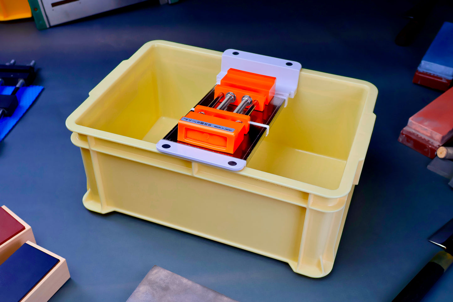 tall yellow knife sharpening box rectangular shaped with suehiro multi sliding rack white and silver with orange rubber whetstone holder surrounded by knife sharpening accessories on dark blue grey surface