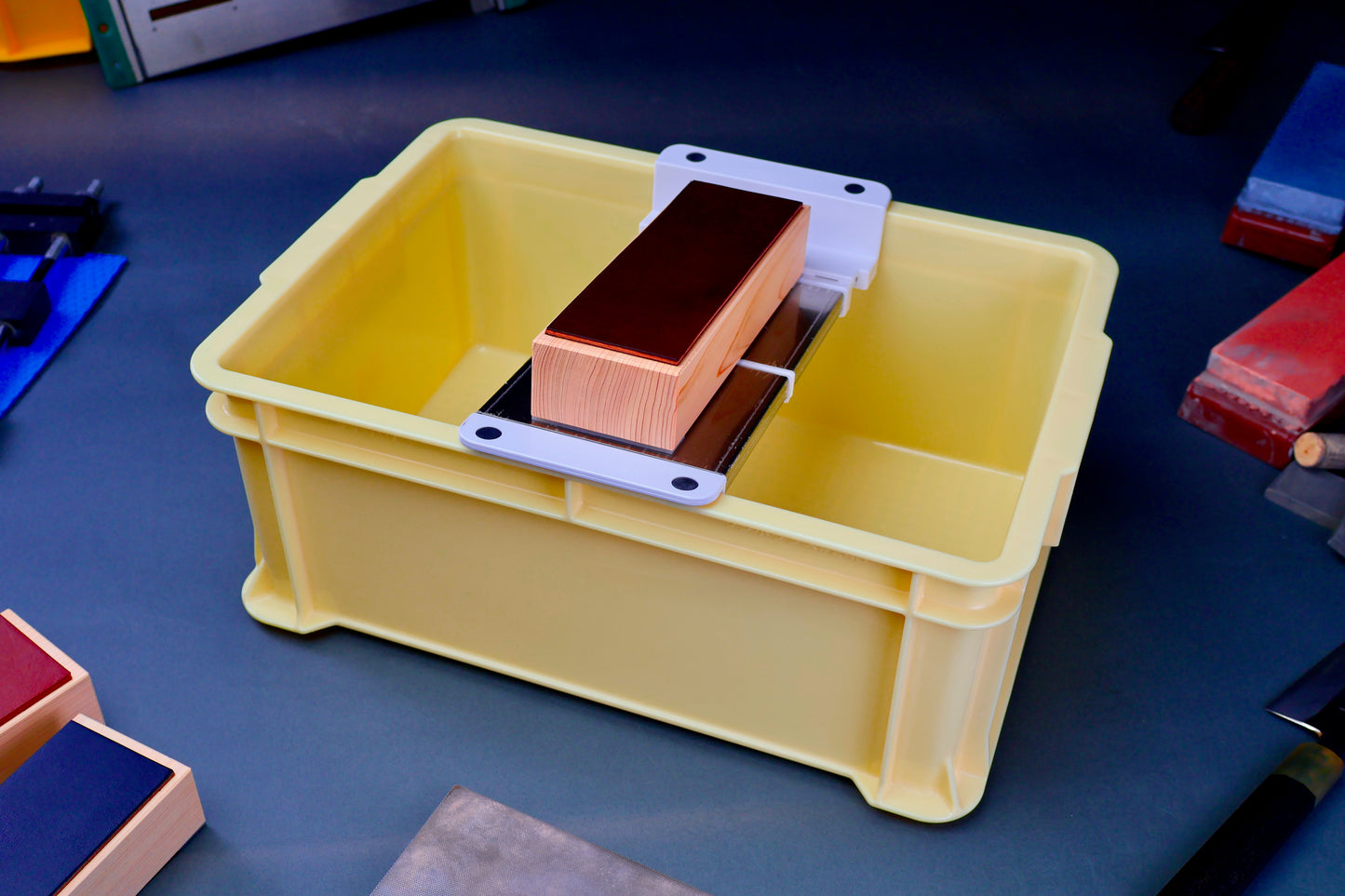 tall yellow knife sharpening box rectangular shaped with suehiro multi sliding rack white and silver surrounded by knife sharpening accessories on dark blue grey surface