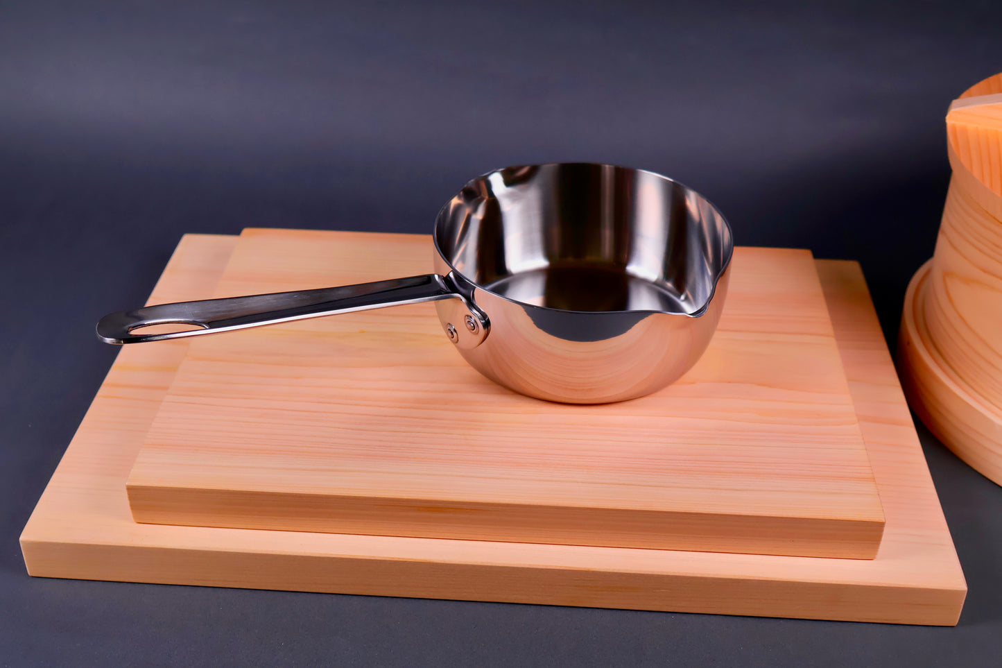 elegant curved shiny body of yukihira saucepan showing rivets of handle on wood cutting boards with grey backdrop