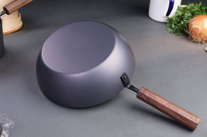 underside of iron pan with wood octagonal handle surrounded by kitchenware and dark grey background
