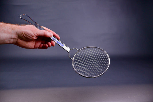 Hand holding a stainless steel coarse strainer with long sturdy handle against a dark background