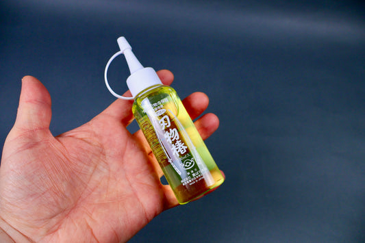 Tsubaki oil made by Kurobaru hand holding plastic bottle with nozzled white cap grey background 