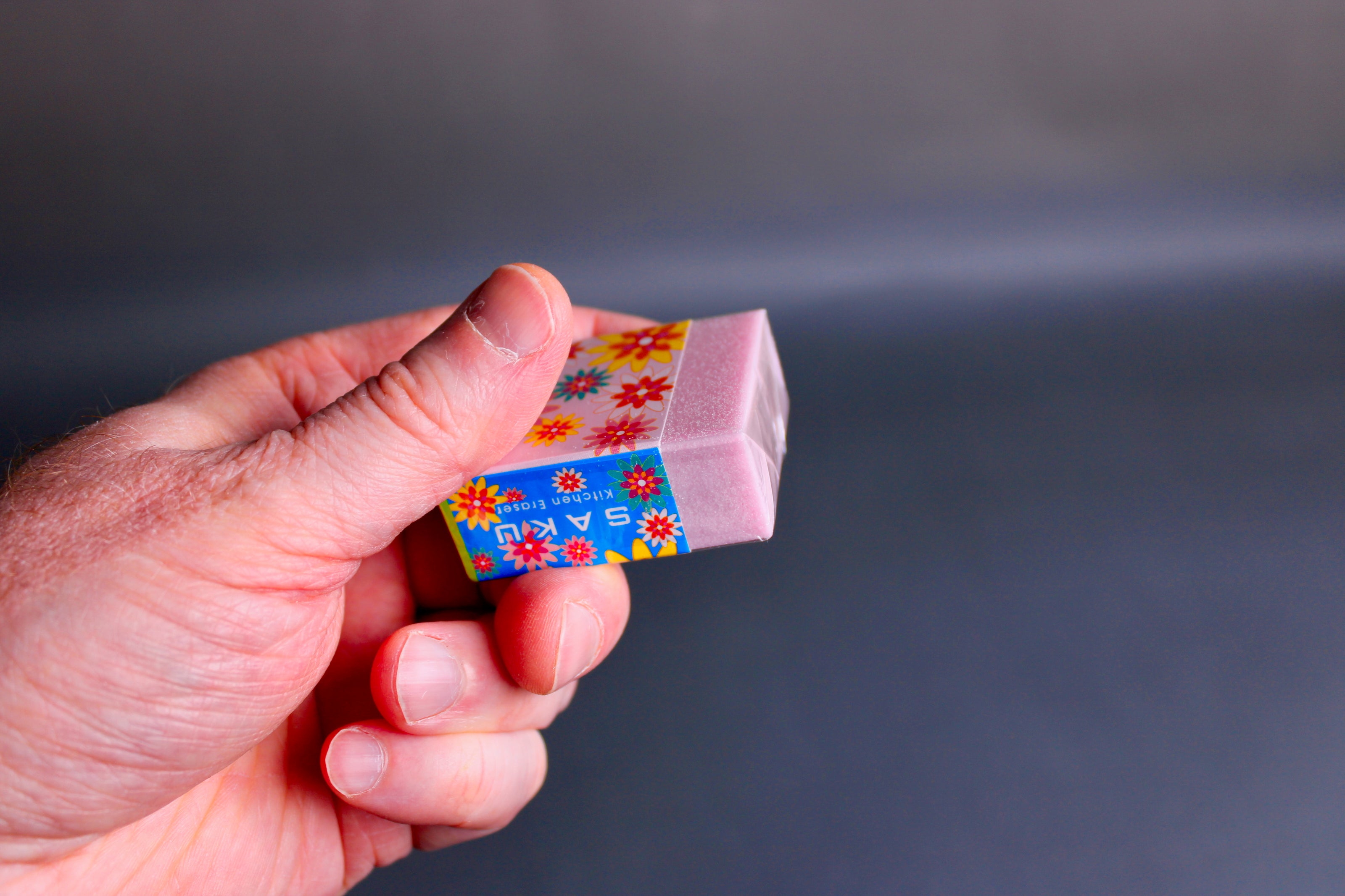 Hand holding a colorful Naniwa rust eraser against a dark background