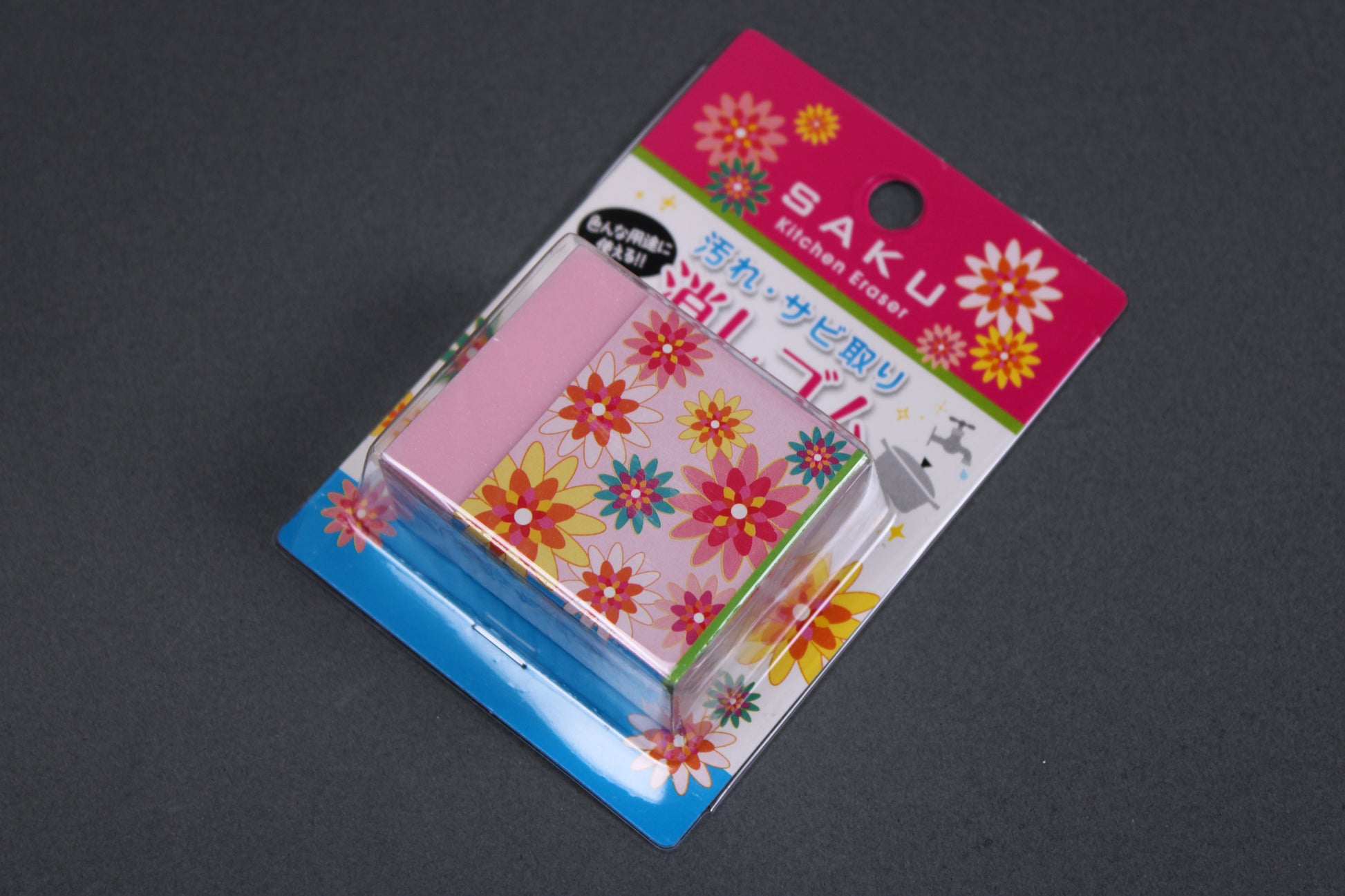 pink block shaped rust eraser partially wrapper in thick paper cover with multicolored star flower shapes in product package with Saku 