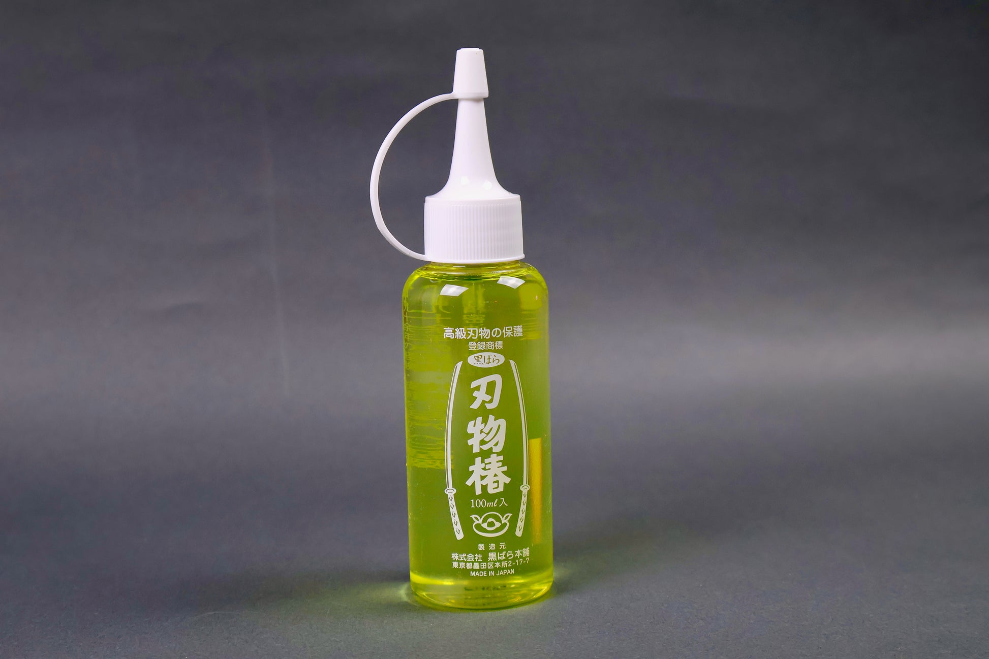 clear plastic 100ml dispenser bottle with looped white cap yellowish gold oil showing white print on container with sword animations and hiragana grey background