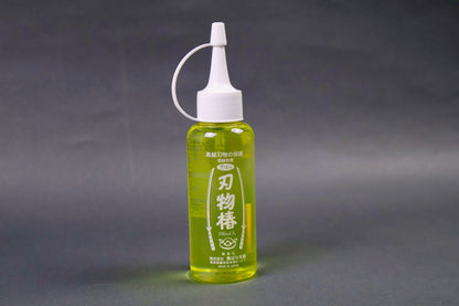 clear plastic 100ml dispenser bottle with looped white cap yellowish gold oil showing white print on container with sword animations and hiragana grey background