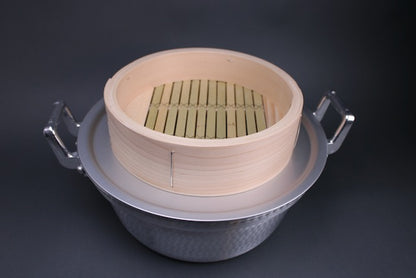 bamboo and kiso hinoki wood chinese steamer base sitting atop aluminum steam ring and steaming pot made of aluminum with hammered surface and two handles top down view with grey background  