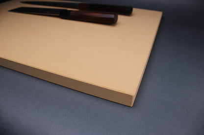 detailed close up shot of Asahi cutting board surface and beveled corners with two japanese knives atop the board in the background with a grey backdrop