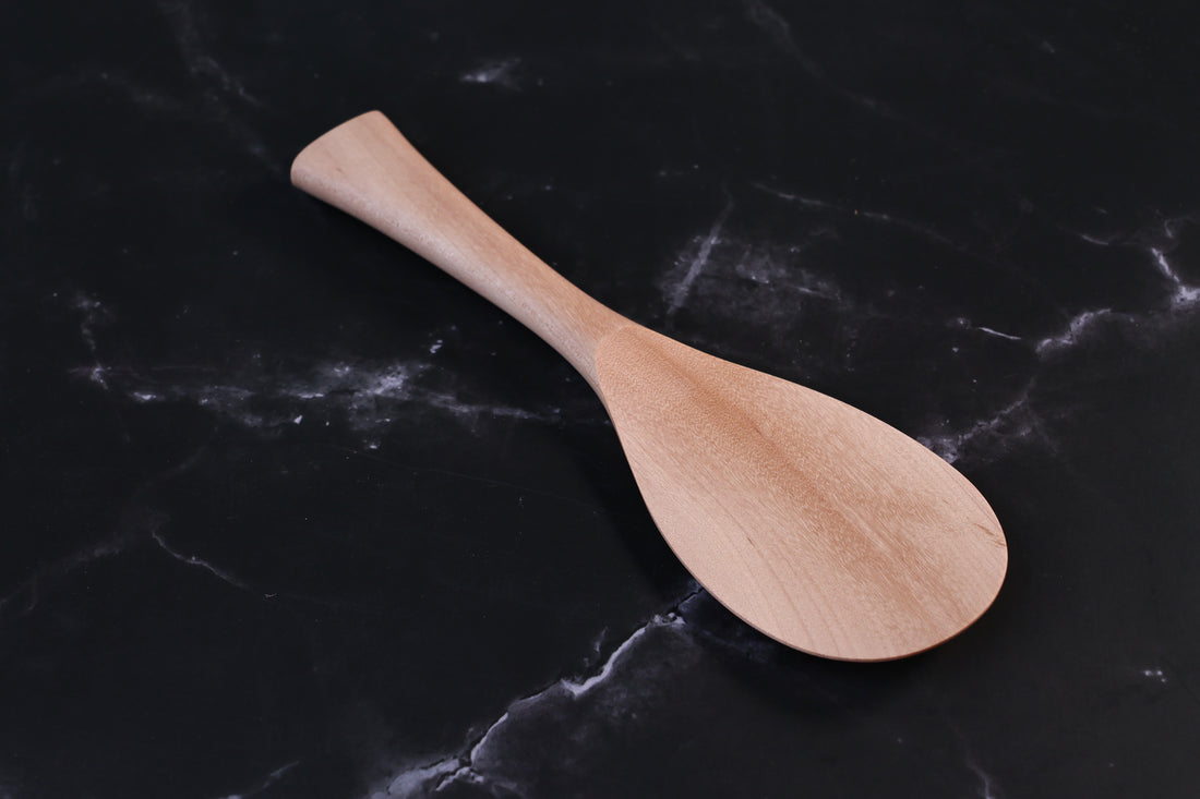 Azmaya handmade maple rice paddle in size L shown front-on at an angle on a dark marble surface
