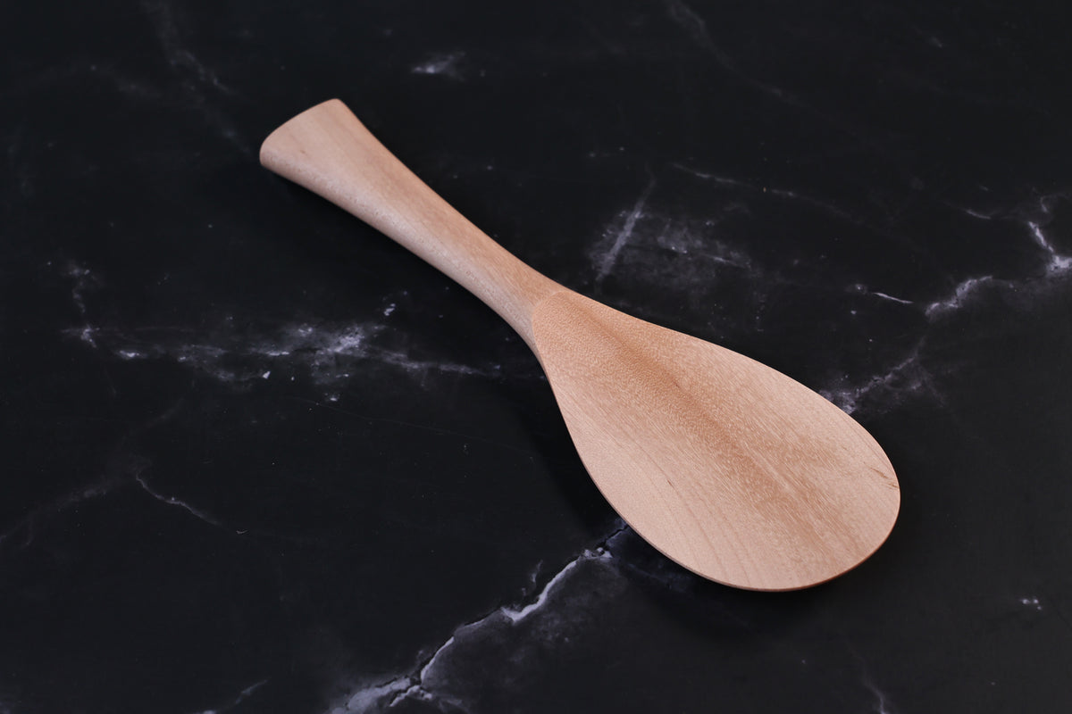 Azmaya handmade maple rice paddle in size L shown front-on at an angle on a dark marble surface