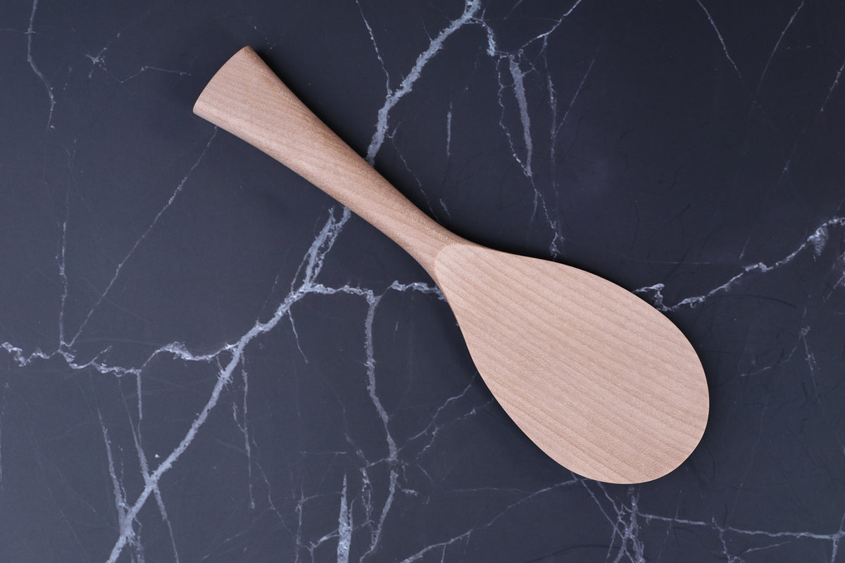 Azmaya handmade rice paddle overhead view on black marble showing natural wood grain and paddle shape