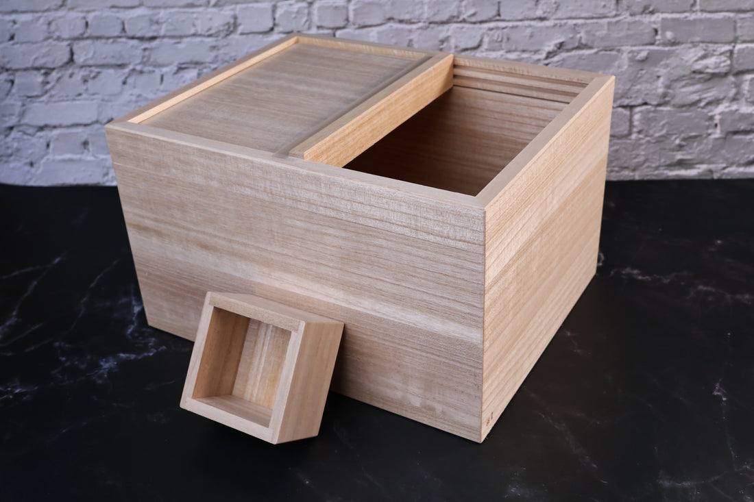 Azmaya kiri wood rice bin with one lid panel slid open and the masu measuring cup resting beside it