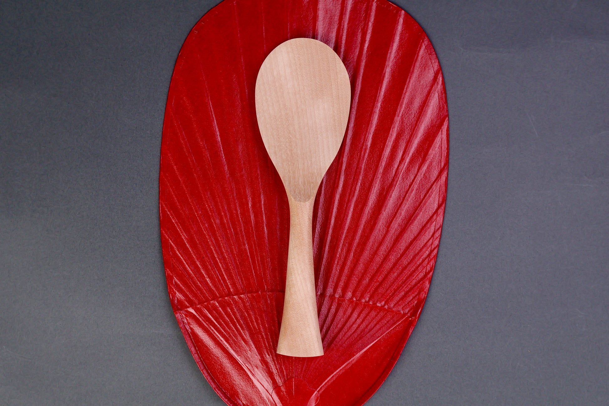 hand carved wooden rice paddle light golden brown yellowish tone of paddle atop deep red background surface